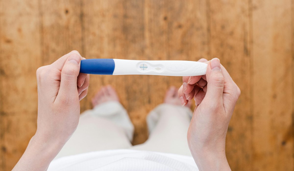 Overhead view of a woman holding a positive pregnancy test indoors.