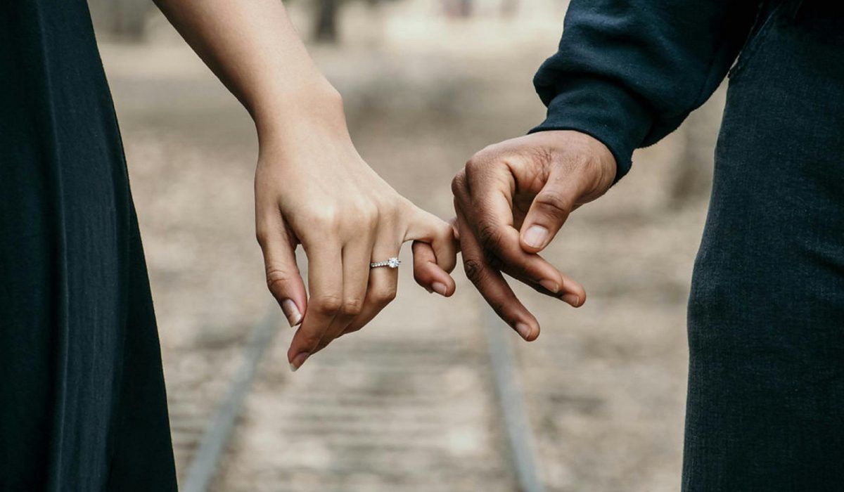 A romantic couple holding hands, symbolizing love and unity on a scenic railtrack.